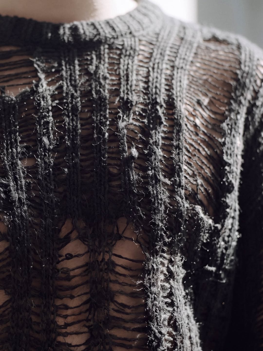 Close-up of a distressed black open-knit sweater in raking light.